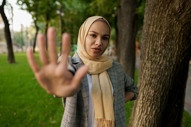 Arabisch meisje in hijab toont haar handpalm in zomerpark. moslimvrouw met boeken die op het gazon op de universiteitscampus rusten.