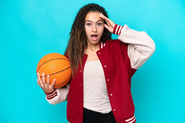 Arabische basketbalspelervrouw die op blauwe achtergrond met verrassingsuitdrukking wordt geïsoleerd