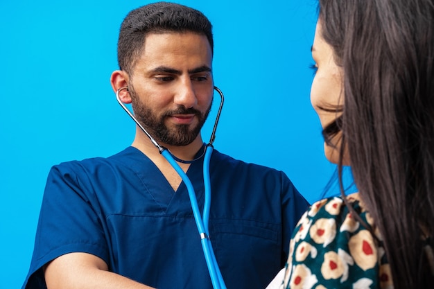 Arabische dokter in een blauw uniform staat met de stethoscoop en luistert naar de hartslag van een vrouw...