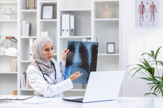 Arabische islamitische vrouwelijke dokter bezorgd zit aan het bureau in het kantoor voor de laptop doen online