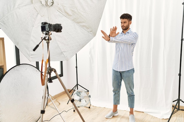 Arabische jonge man die zich voordeed als model bij fotostudio afwijzing uitdrukking kruisen armen en handpalmen doen negatief teken boos gezicht