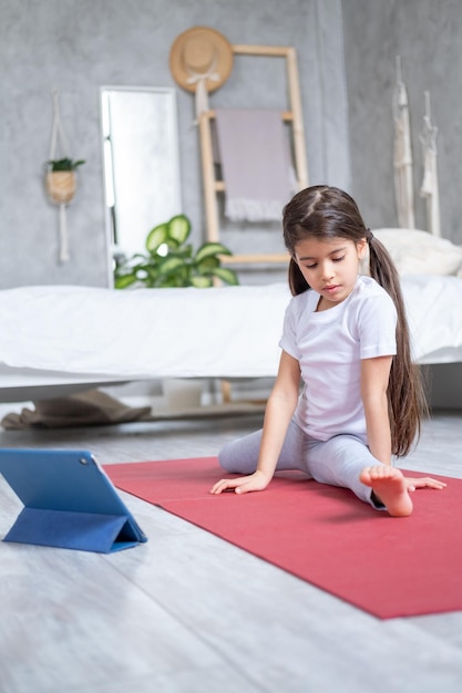 Arabische jongen doet stretching online oefenen met tablet op fitnessmat thuis in modern appartement