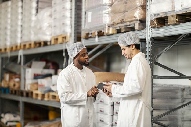 Arabische magazijnmanager met tablet bepaalt taken voor zijn zwarte werknemer in de faciliteit