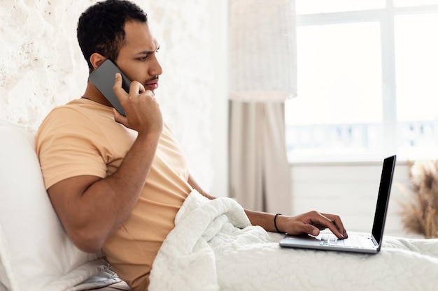 Arabische man die aan de telefoon praat met een laptop die in de slaapkamer werkt