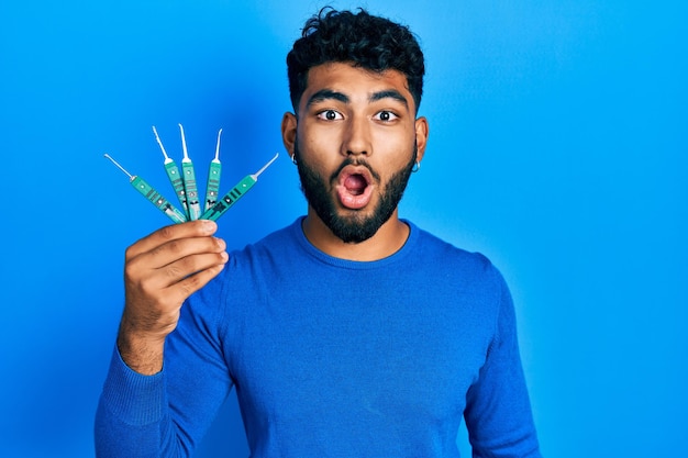 Arabische man met baard die picklock vasthoudt om de veiligheidsdeur te openen, bang en verbaasd met open mond voor een verrassend ongeloof gezicht