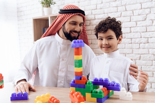 Arabische man met jongen bouwt toren van gekleurde plastic blokken.