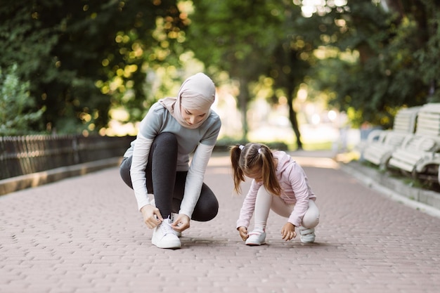 Arabische moeder en haar dochter passen sneakers aan die op de joggingbaan in het park zitten