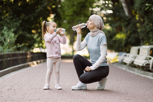 Arabische moeder kijkt naar haar dochter en drinkt water terwijl ze rust na een sporttraining buitenshuis