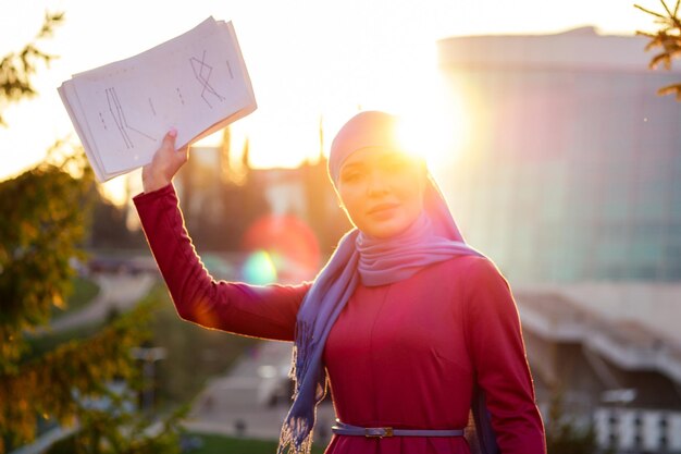 Arabische moslim zakenvrouw hijab met make-up staande op straat met documenten en papieren op een achtergrond van zomer park. vrouw is gekleed in een stijlvolle abaya en sjaal. succesvol dealconcept