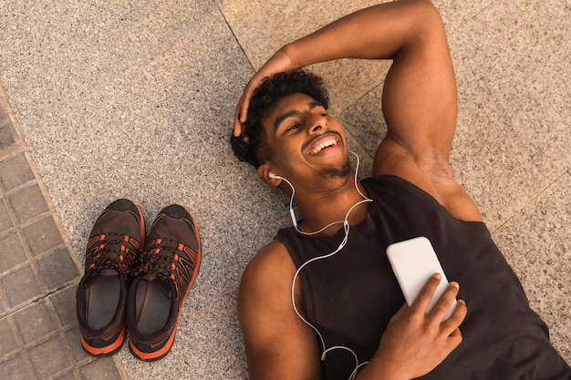 Arabische sterke jonge man rust na sport in de stad liggend op de grond glimlachend