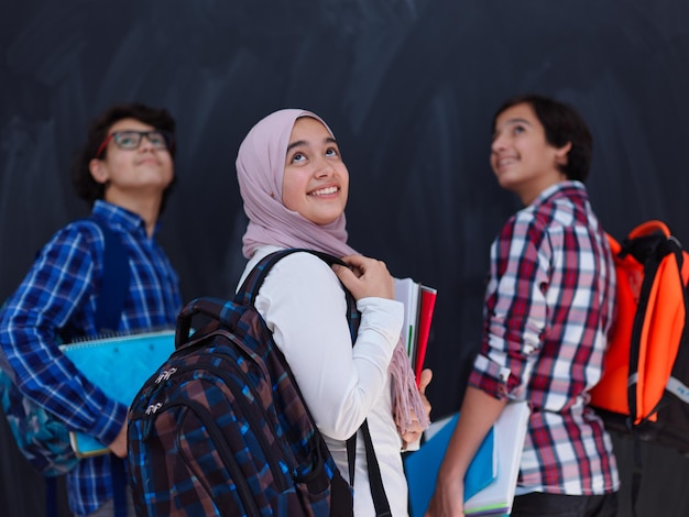 Arabische tieners, studentengroepsportret tegen zwart bord met rugzak en boeken op school