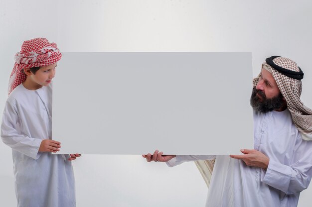 Arabische vader met zoon die een witte poster vasthoudt en zijn tong uitsteekt stock foto