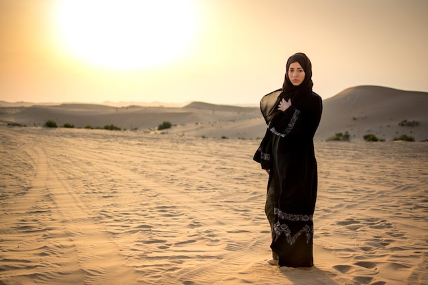 Arabische vrouw die tijdens de zonsondergang in de woestijn staat