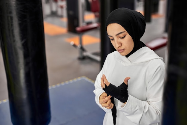 Arabische vrouw kickbokser in hijab bindt een zwarte elastische bandage op haar hand voordat ze alleen vecht en traint in de sportschool