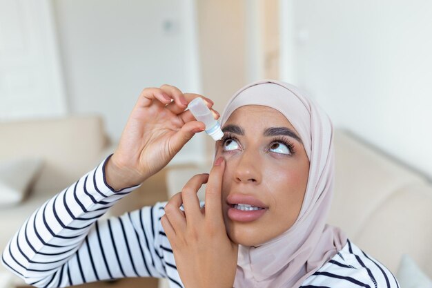 Arabische vrouw met hijab die oogdruppels gebruikt die oogsmeermiddel gebruiken om droge ogen of allergie te behandelen Zieke vrouw die oogbalirritatie of -ontsteking behandelt Vrouw die lijdt aan geïrriteerde optische symptomen van het oog