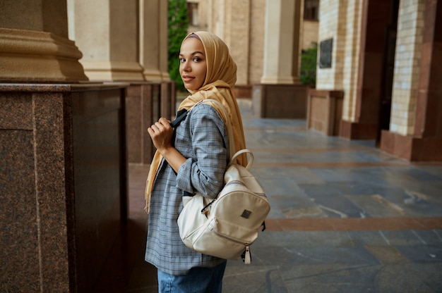 Arabische vrouwelijke student met boeken bij de ingang van de universiteit. Moslimvrouw in hijab houdt schoolboeken buiten.