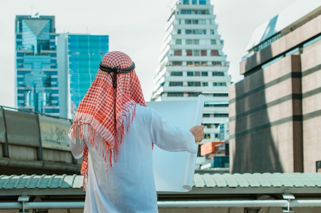 Arabische zakenman die met blauwdruk wegkijkt