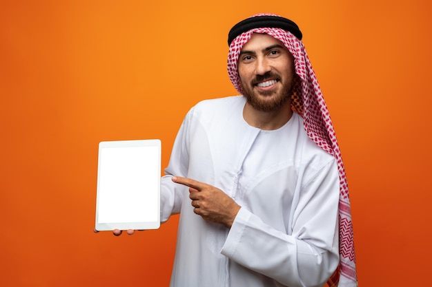 Arabische zakenman in traditionele kleding die lege digitale tablet toont tegen oranje achtergrond