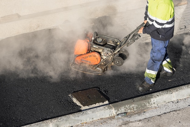 Arbeider met een trilplaatpersmachine die aan een stadsstraat werkt