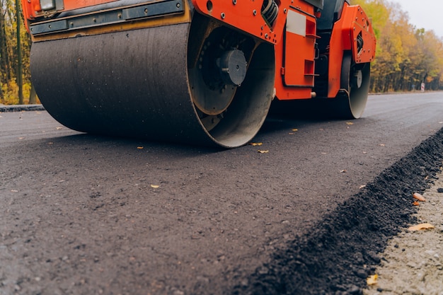 Arbeiders die de machine van de asfaltbetonmolen in werking stellen tijdens wegenbouw. Dichte mening over de wegwals die aan de nieuwe wegenbouwplaats werkt.