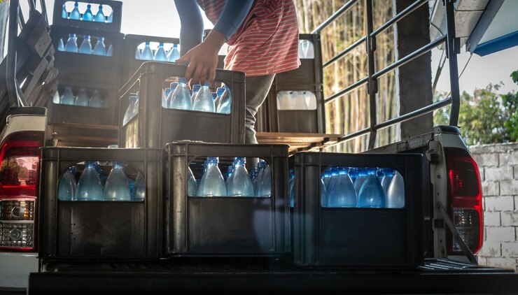 Arbeiders tillen blauwe drinkwaterflessen in kratten achter in een transportwagen
