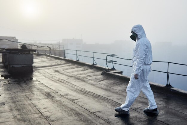 Arbeiderswetenschapper die beschermende overall en gasmasker draagt die ecologische tests op het dak doen