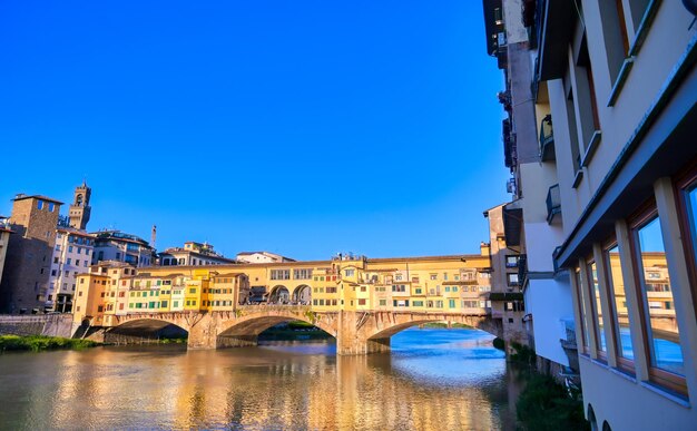 Arch bridge over river by buildings against clear blue sky