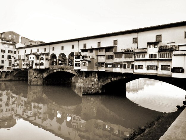 Arch bridge over river by buildings against clear sky