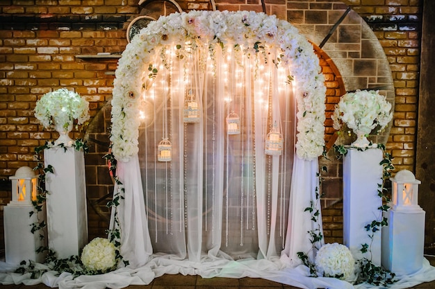Арка для свадебной зоны декорирована белыми цветами и зеленью. Свадебная церемония со старинными свечами.