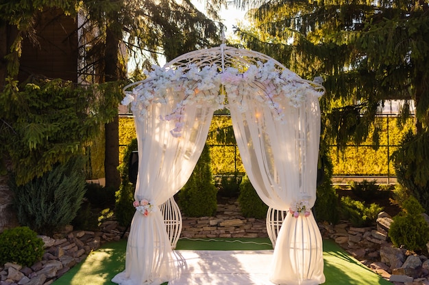 Arch for the wedding ceremony decorated with cloth flowers and greenery is in a pine forest