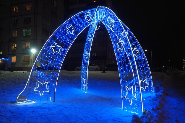 Arch with blue street garlands Festive background Blue and white light bulbs as a decoration for the New Year and Christmas night Street decoration design Abstract light spots Star shape