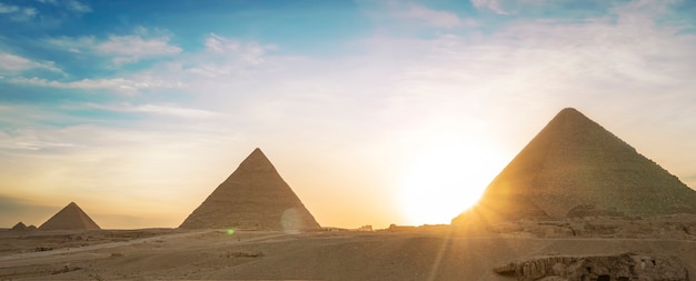 Archaeological complex of the Great Egyptian Pyramids is located on the Giza plateau. Pyramids of Chephren Khafra and Cheops Khufu in the night light at sunset. sun sets behind the pyramid.