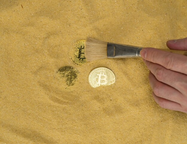 An archaeologist with a brush clears the bitcoin coin on the golden sand Mining cryptocurrency