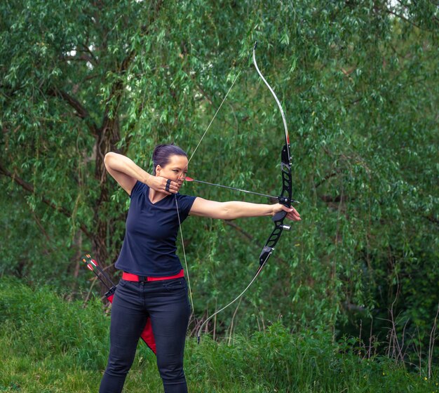 Tiro con l'arco in natura. una giovane donna attraente si sta allenando in un tiro con l'arco con una freccia a un bersaglio nel bosco