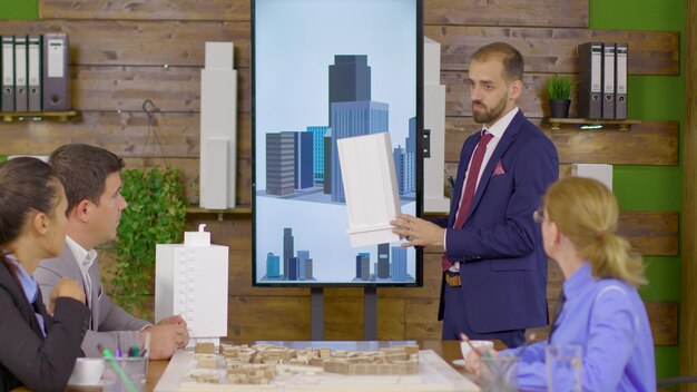 Photo architect in business suit holding a presentation about new building project. architect holding building model. mini town.