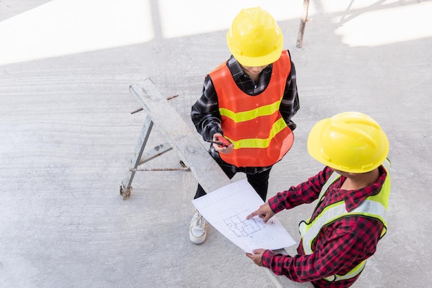 Architect and client discussing help create plan with blueprint of the building at construction site floor. Asian engineer foreman worker man and woman meeting and planning construction work, top view