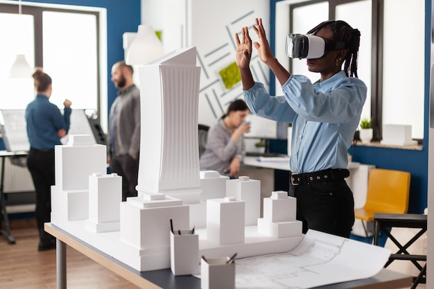 Architect die met virtual reality-bril werkt om naar witte schuimmaquette van het bouwcomplex van kantoorgebouwen te kijken. Ingenieur die toekomstige innovatie in architectenbureau gebruikt.