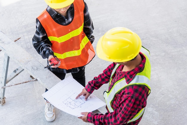 Architect en klant bespreken hulp bij het maken van een plan met blauwdruk van het gebouw op de bouwplaatsvloer Aziatische ingenieur voorman werknemer man en vrouw ontmoeten en plannen bouwwerkzaamheden bovenaanzicht