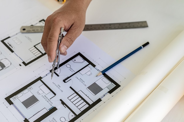 Architect engineer using compasses to write on the blueprints\
they have designed, he is checking and revising the drawings before\
submitting the work to the customers. design and interior design\
ideas