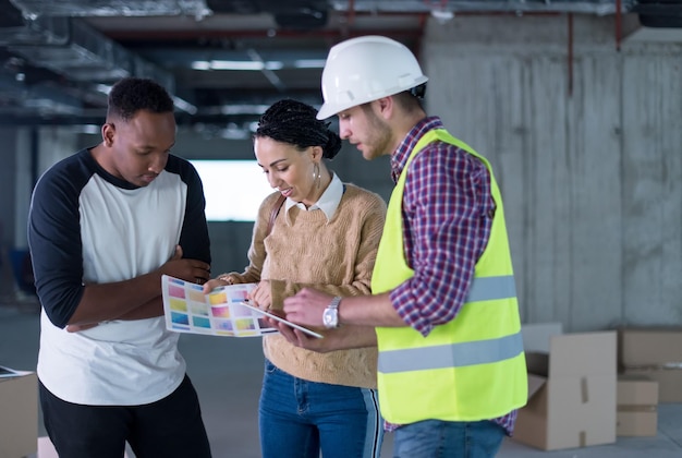 architect engineer using tablet computer while showing house design plans to a young multiethnic couple at construction site