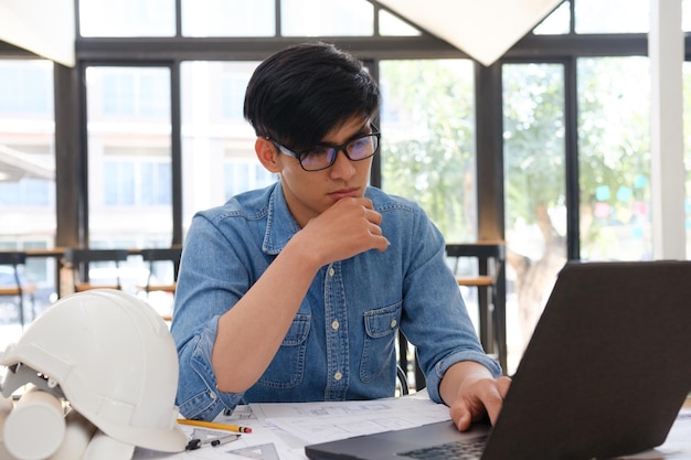 architect and engineer working on a laptop with blueprints at a desk in an office