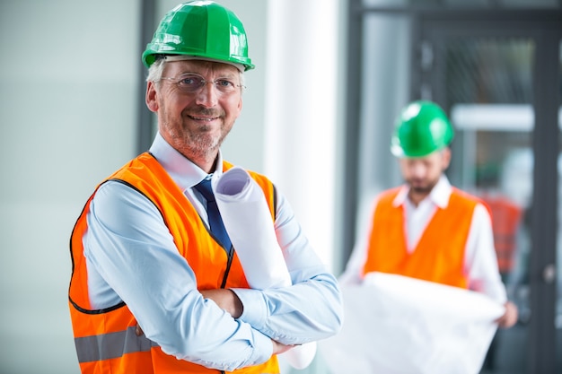 Architect in hard hat standing with blueprint in office corridor