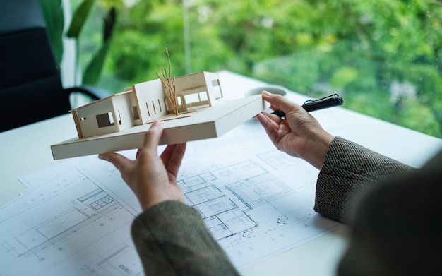 An architect holding and working on an architecture house model with shop drawing paper in the office