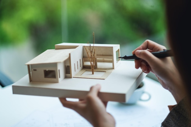 An architect holding and working on an architecture house model with shop drawing paper in the office