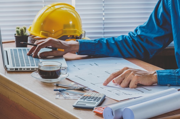 Architect man hand working with laptop and blueprint on architectural project in office.