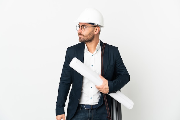 Architect man with helmet and holding blueprints isolated on white background looking to the side