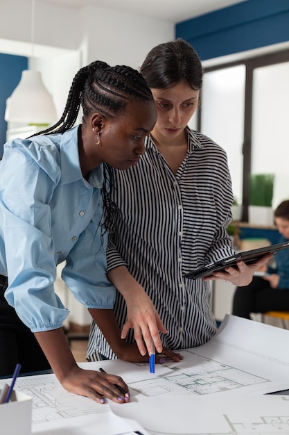 Architect met digitale tabletcomputer met bouwplannen die blauwdrukken uitleggen aan Afro-Amerikaanse ingenieurscollega. Professionele architecten in architectenbureau die stedelijke ontwikkeling ontwerpen