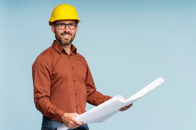 architect of ingenieur met een gele hardhat die een architectonische tekening op de achtergrond vasthoudt