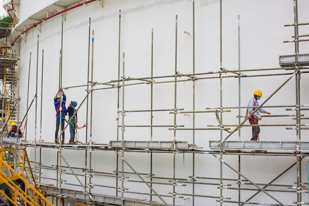 Architect on site construction workers on a scaffold tank oil. Extensive scaffolding providing platforms for work in progress. Men walking on roof surrounded by scaffold