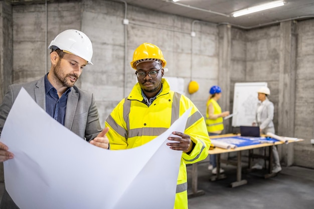 Architect and structural engineer looking at building plan or blueprint at construction site